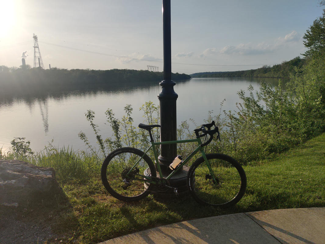 Lime green gravel bike leaning against a light post. Sunset over the river in the background.
